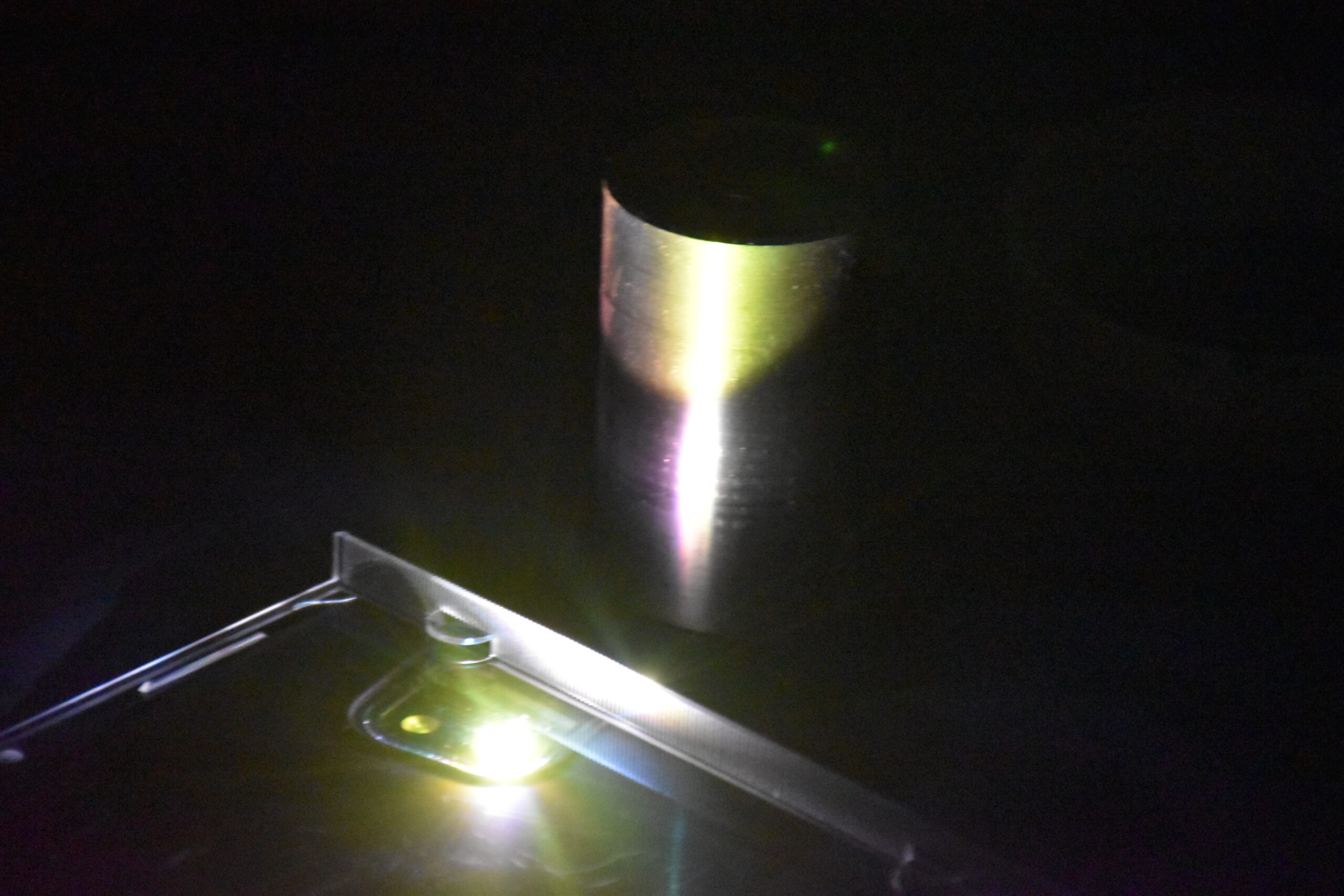 Green LED Light from my phone under a CD case, reflecting off a brushed aluminium cylinder.